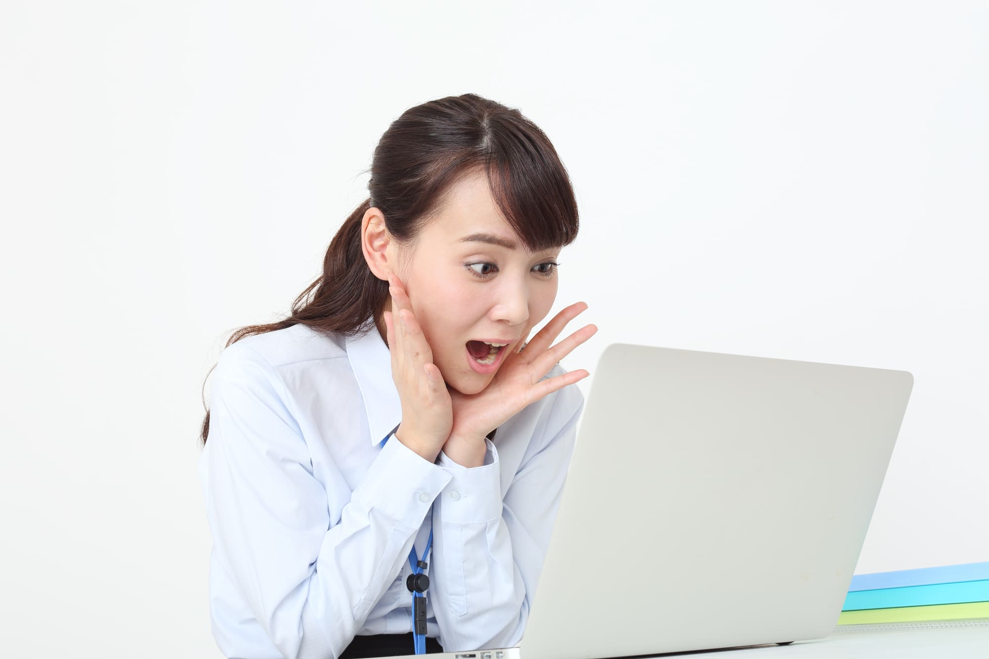 ノートパソコンの前で驚く白いシャツを着た女性